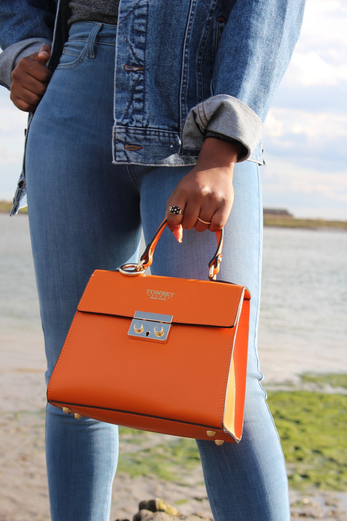 Lady in jean holding orange Kelly Bovine Leather bag