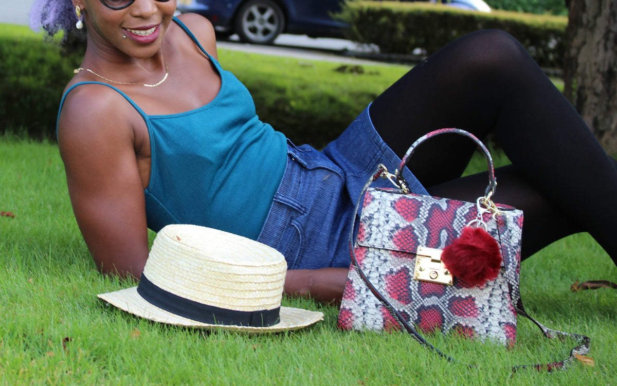 Red snake embossed leather bag with model laying on grass